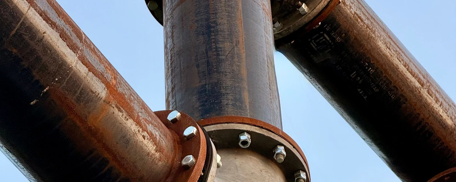 Large rusted pipes with bolted flanges against a blue sky