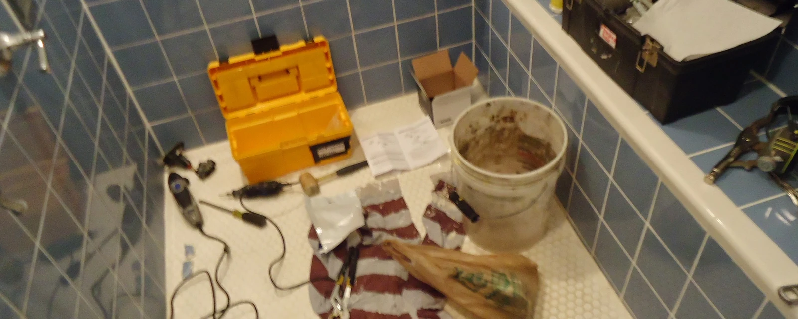 Yellow toolbox, tools and a bucket on a tiled bathroom floor during a plumbing job
