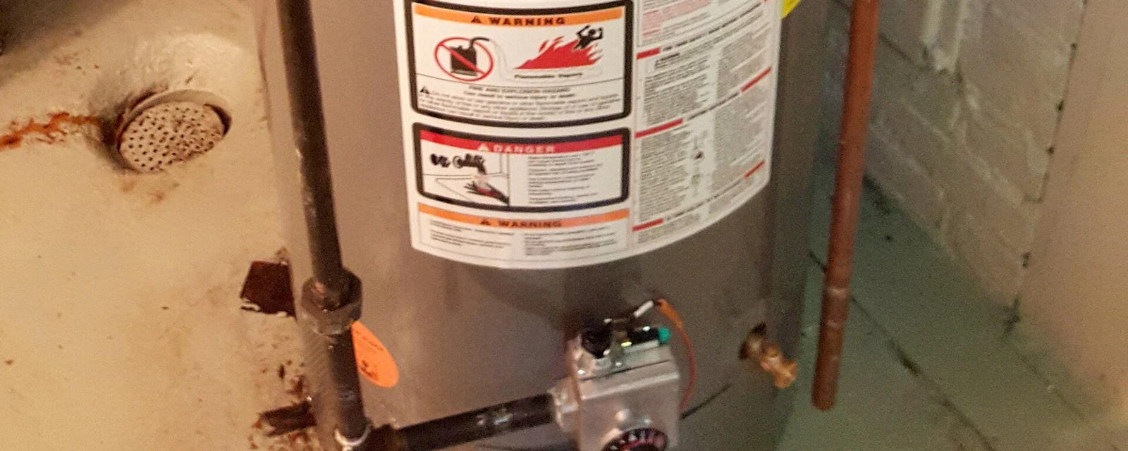 Lower half of a gas tank water heater with warning labels, a gas valve and copper pipe